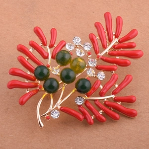 Détail macro d'une broche corail dorée avec émail rouge et perles vert foncé