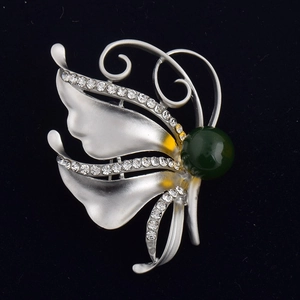 Détail macro d'une broche papillon argentée avec pierre verte et zircons clairs