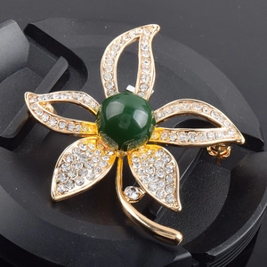 Makrodetail einer Blumenbrosche mit Goldblättern, weißen Kristallen und grünem Stein