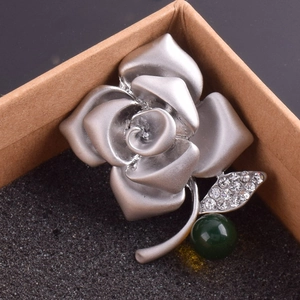 Detailed close-up of a silver rose flower brooch with rhinestones and a green bead inlay