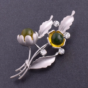 Nahaufnahme einer Vintage-Blumenbrosche mit mattem Silberfinish und grünen Kristallperlen