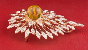 Detail view of gold vintage brooch with yellow amber stone and radiant leaf patterns