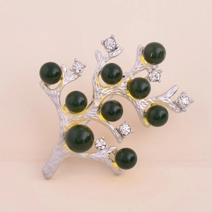 Détail d'une broche branche argentée avec perles vertes et strass sur fond rose