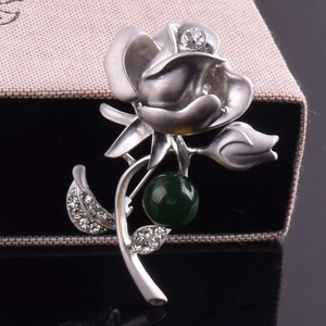 Vue détaillée de la broche rose argentée avec cristaux et perle verte sur boîte cadeau