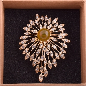 Close-up of golden sunflower brooch with green center stone and sparkling crystals
