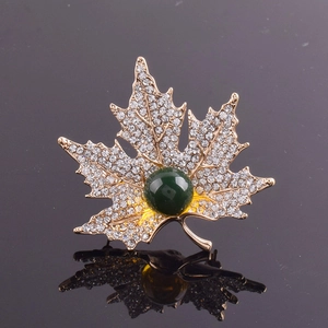Détail d'une broche en forme de feuille d'érable dorée avec cristaux blancs et pierre verte