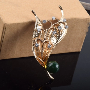 Dettaglio della spilla a mughetto con petali dorati e una grande perla verde