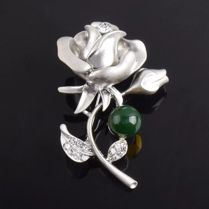 Détail macro d'une broche fleur argentée avec perle verte et pétales sertis de cristaux
