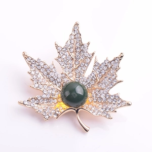 Détail de la broche feuille d'érable dorée avec cristaux et pierre gemme verte