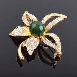Makro-Detail der goldenen Blumenbrosche mit weißen Kristallen und grüner Perle
