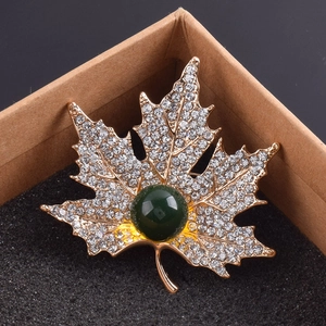 Détail de la broche feuille d'érable en or rose avec cristaux blancs et perle verte