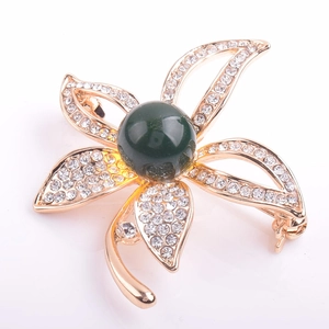 Detailaufnahme einer Blumenbrosche aus Goldlegierung mit Kristallen und dunkelgrüner Perle
