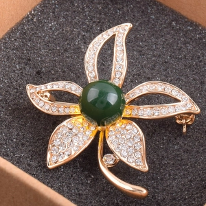 Nahaufnahme goldene Blumenbrosche mit weißen Kristallen und großer dunkelgrüner Perle