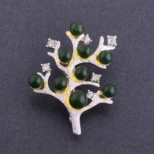 Vue détaillée d'une broche en forme de branche avec perles d'ambre vert et cristaux blancs