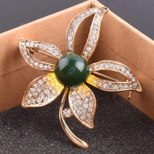 Makroaufnahme der goldenen Blumenbrosche mit weißen Kristallen und grüner Perle