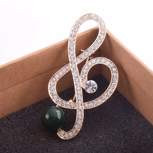 Close-up of a musical treble clef brooch with rhinestones and a large green pearl