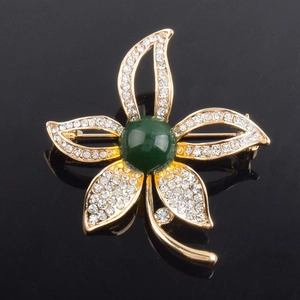 Makroaufnahme einer Blumenbrosche aus Goldlegierung, weißen Strasssteinen und grünem Stein