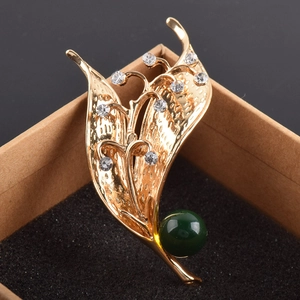 Dettaglio della spilla a mughetto dorata con strass bianchi e perla verde scuro