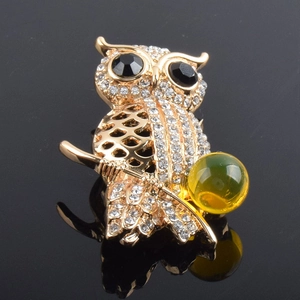 Detailed close-up of a golden owl brooch with crystal rhinestones on a black mirror surface