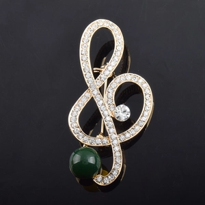 Detail of music note brooch with crystals and a large green pearl on black background