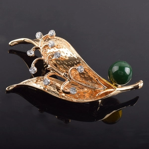 Primo piano dettagliato di una spilla a mughetto con accenti di cristallo e pietra verde