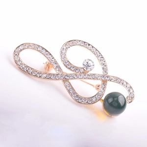 Macro detail of gold-plated spiral brooch with white crystals and a dark green bead accent