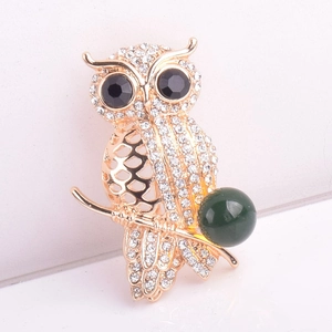 Macro shot of owl brooch with crystals and green bead on gold branch detail