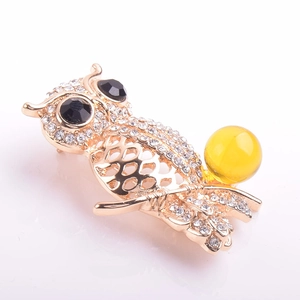 Macro detail of owl brooch showing gold metal craft, sparkling rhinestones and amber bead