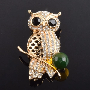 Detailed close-up of a gold owl brooch featuring white rhinestones and a large green gem