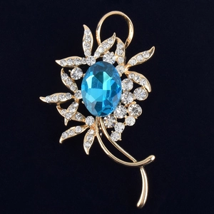 Gros plan sur une broche fleur dorée avec grand cristal bleu et strass blancs brillants