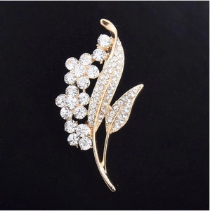 Elegant gold flower brooch with white crystals and rhinestones on black background