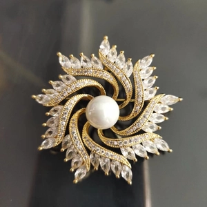 Macro shot of luxury gold windmill brooch featuring a pearl center and sparkling zircon stones