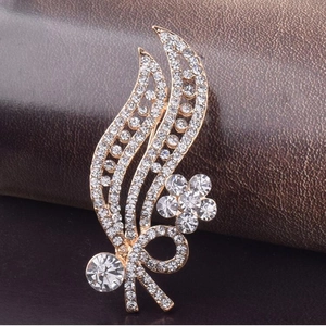 Elegant gold leaf brooch with white rhinestones and ribbon detail on leather surface