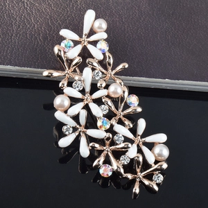 Détail macro d'une broche fleurie avec pétales en émail blanc, perles et strass