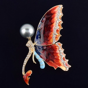 Detailed close-up of butterfly brooch with orange enamel wings and grey pearl on black background