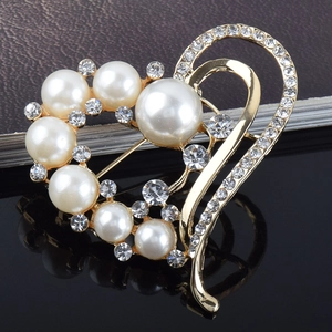 Broche cœur dorée élégante avec perles et strass sur une surface noire réfléchissante