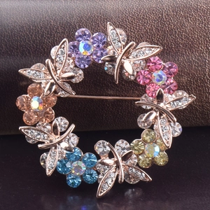 Detail of a floral wreath brooch with colorful rhinestones and a dragonfly on rose gold base