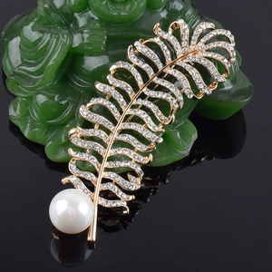 Gros plan d'une broche plume avec strass blancs et perle sur un support doré élégant