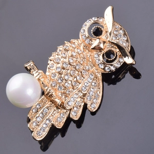Eleganter goldener Eulen-Anstecknadel mit Kristallen und Perle auf dunklem Spiegelgrund