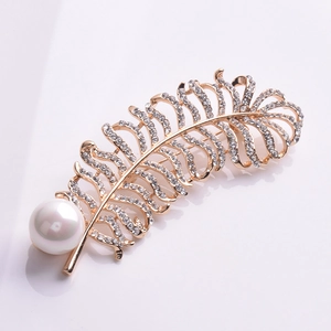 Détail d'une broche en forme de plume dorée avec cristaux brillants et perle blanche