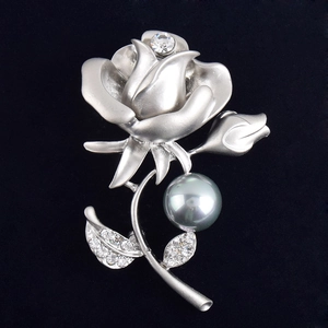 Détail macro d'une broche rose avec pétales argent mat, perle grise et cristaux brillants