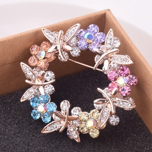 Detailed close-up of a rose gold dragonfly and colorful crystal floral brooch