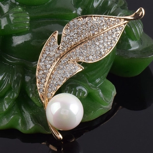Détail d'une broche feuille dorée avec cristaux blancs et une perle sur fond vert