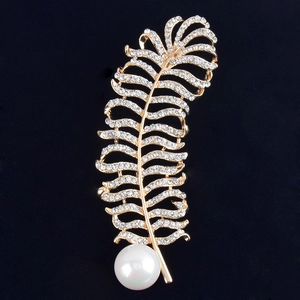 Détail d'une broche en forme de plume dorée avec cristaux brillants et une perle blanche