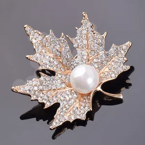 Close-up of golden maple leaf brooch with sparkling crystals and a large white pearl