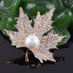 Detail of maple leaf brooch with sparkling rhinestones and a white pearl on golden base