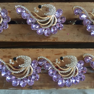 Dettaglio di spilla a pavone dorata con cristalli viola a goccia e strass scintillanti