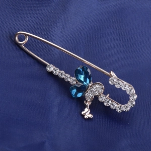 Detail of a gold safety pin brooch featuring a blue gemstone butterfly and clear zircons