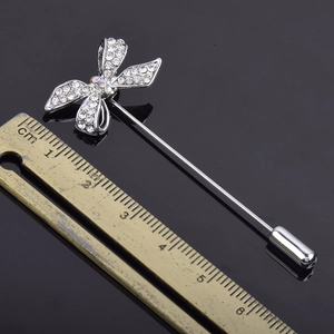 Broche nœud argentée étincelante avec strass et longue épingle présentée avec une règle