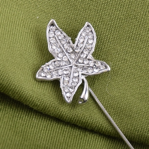 Elegant maple leaf crystal brooch with silver finish and pearls on green fabric background
